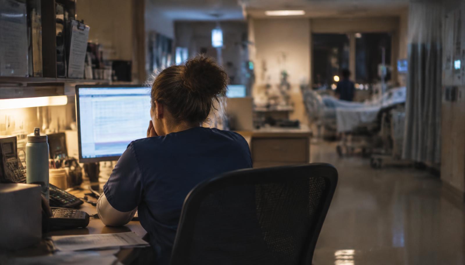 A nurse working at a dimly lit hospital nurses' station during a night shift